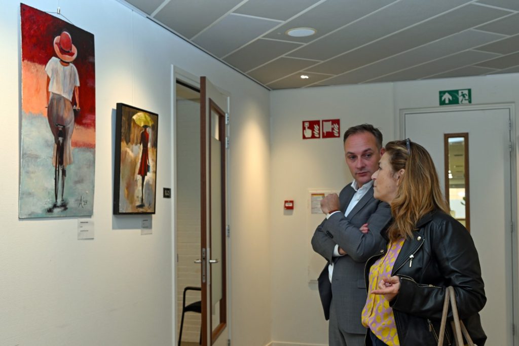 wethouder Phillipe van Ham staat voor een schilderij en is in gesprek met een vrouw