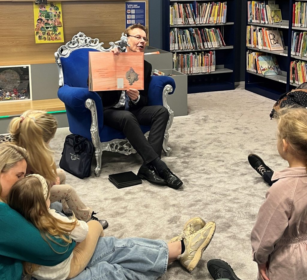 Burgemeester Ronald Wortelboer zit in de bibliotheek en laat een pagina van prentenboek 'Rinus' zien aan de kinderen. 