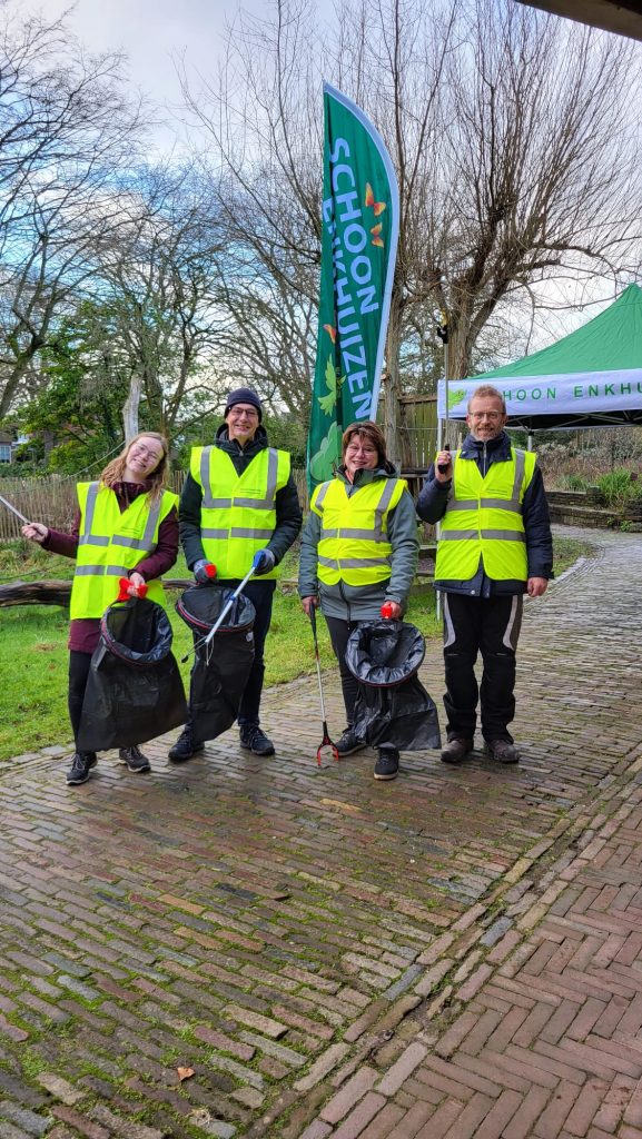 vrijwilligers in gele hesjes, met vuilniszakken en opraapstokken voor afval in de hand.