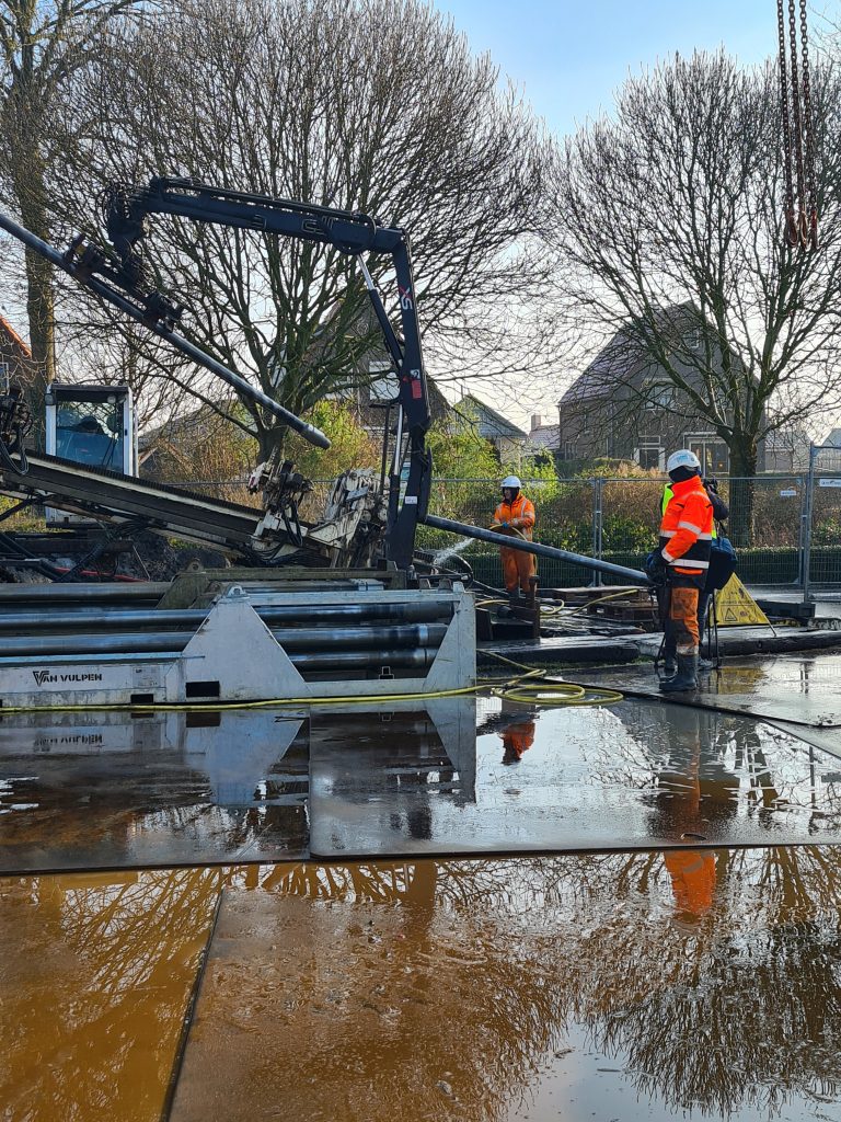 De persleiding wordt onder de grond gestuurd. Op de foto staan twee mannen bij de leiding