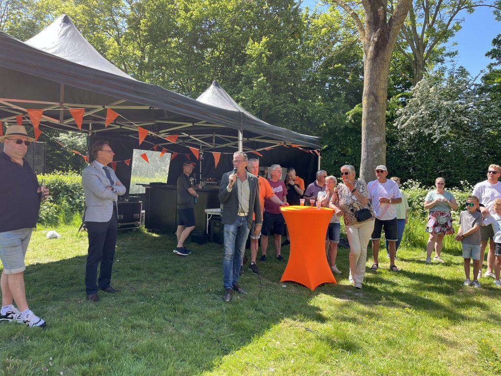 Wethouder Nico Slagter en burgemeester Ronald Wortelboer praten naar de leden van VV Simokos op een grasveld met 2 tenten achter hen.