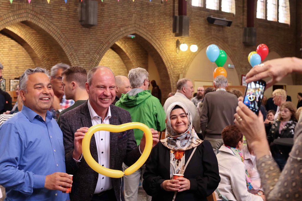 Burgemeester Diepstraten staat met een gele ballon in de vorm van een hart op de foto met twee inwoners naast hem