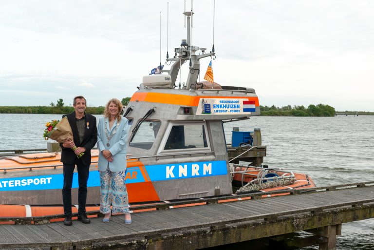 Burgemeester Jeltje Hoekstra-Sikkema staat met meneer Folmer volgens een boot van de KNRM in de haven van Enkhuizen.