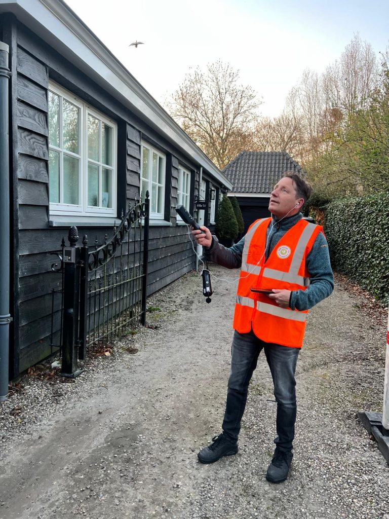 Dave Vonk luistert met een microfoon in de wijk voor het ecologisch onderzoek.