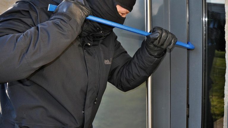 een afbeelding van een inbreker die met een breekijzer een deur met raam probeert te openen
