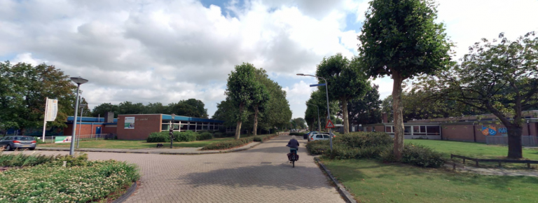 overzicht van de La Reinelaan in bovenkarspel. In het midden de straat met een fietsers, links en rechts bomen. Helemaal links het schoolgebouw