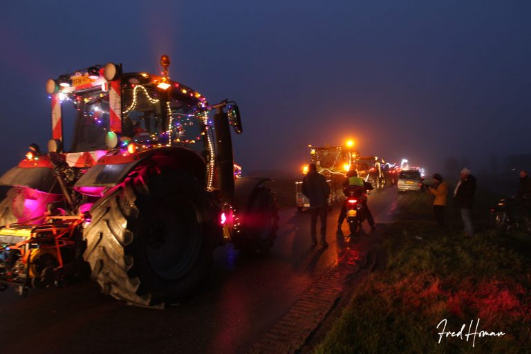 Een trekker links, versierd met lichtjes. Daarvoor, kleiner, nog meer versierde trekkers. Rechts staan wat mensen te kijken, en er staat een motorijder stil.