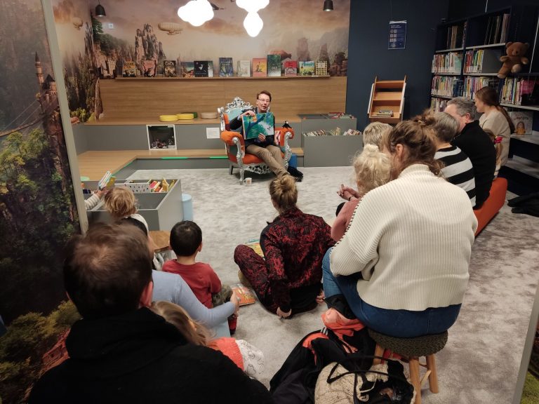 Burgemeester Wortelboer leest voor aan jonge kinderen met hun (groot)ouders.