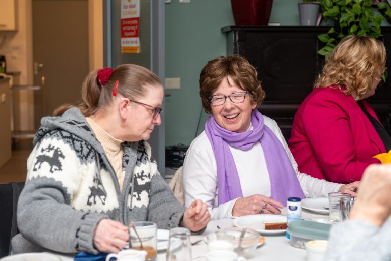 twee vrouwen praten en lachen met elkaar tijdens een lunch.