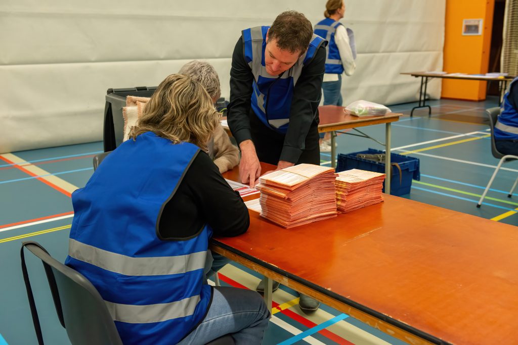 vrijwilligers met een blauw hesje tellen de stemmen