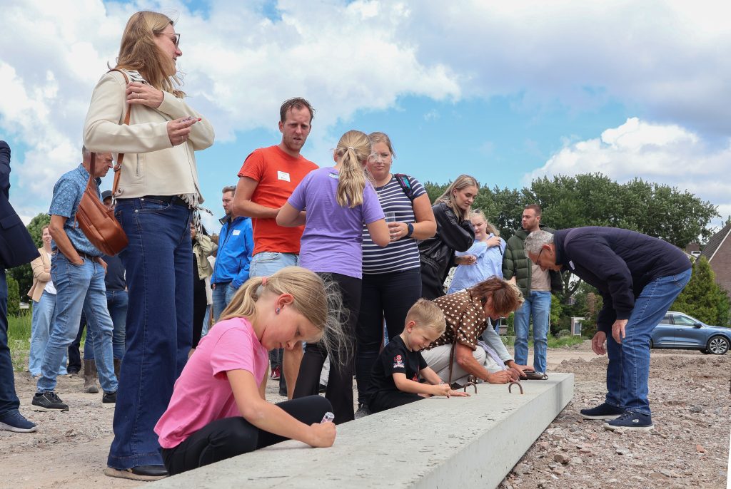 Toekomstige bewoners (zoals gezinnen) tekenen op de betonnen palen die de grond in gaan. 